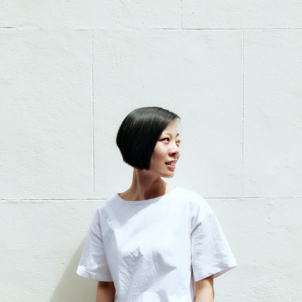 Jingru (Cyan) Cheng stands in front of a white wall and looks to the right.