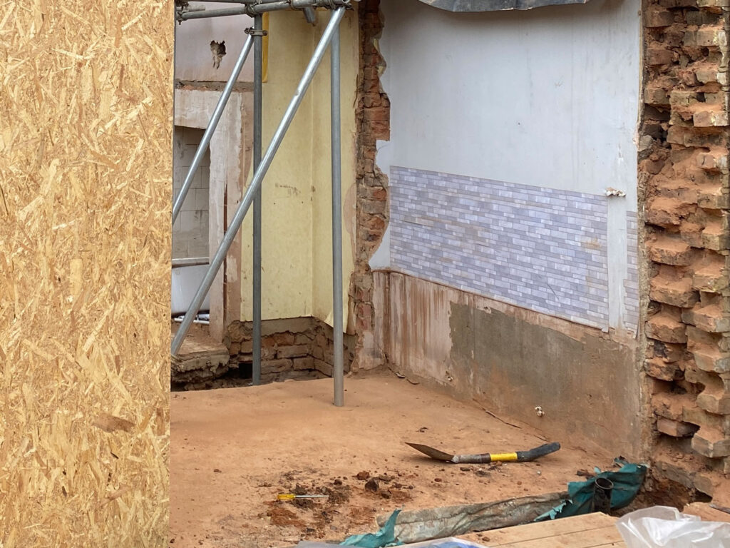 A photograph of a construction site showing a building with scaffolding and a bare floor with a shovel on the ground.